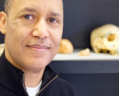 Professor Zeray Alemseged stands in front of a shelf holding fossilized skulls