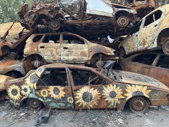 A pile of burned-out cars. The bottom car is painted with a sunflower design.