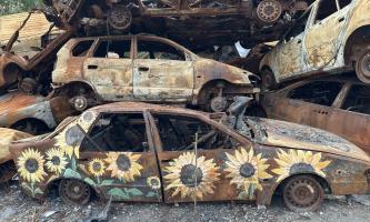 A pile of burned-out cars. The bottom car is painted with a sunflower design.